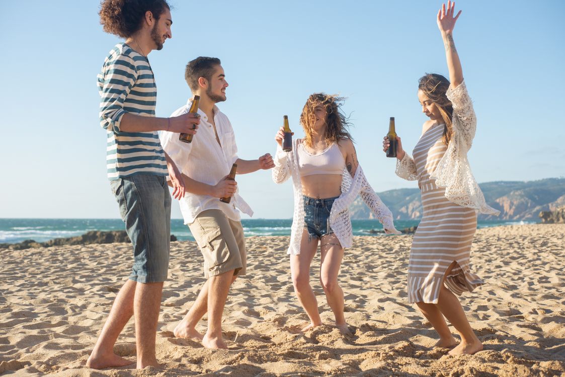 Small group of friends dancing by the shoreline at a sunny European beach destination