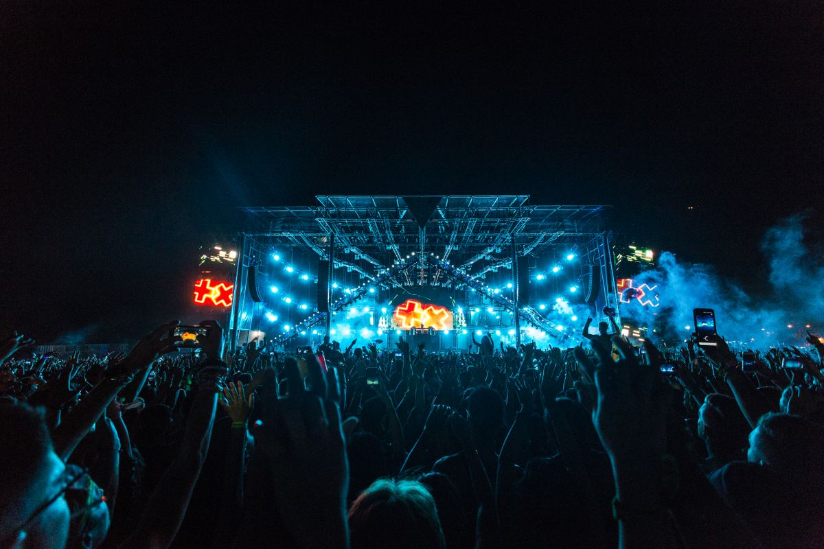 Crowd cheering in front of a blue and orange festival stage at night